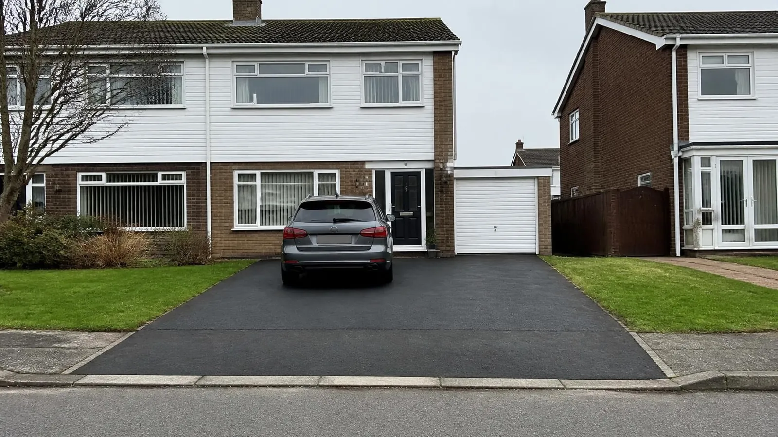1960s semi with a wide new tarmac driveway and an attached garage